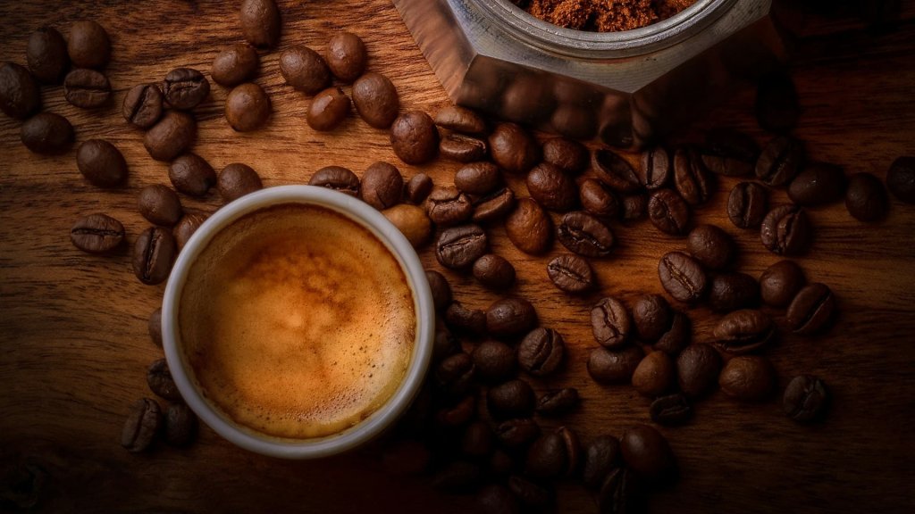Espressokopje op houten tafel tussen versgemalen koffie en bonen, symbool voor een lokaal koffiemoment